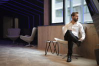 Confident businessman sitting on armchair near window in modern spacious workspace Free Stock Photo