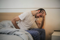Man sitting on bed with a headache.