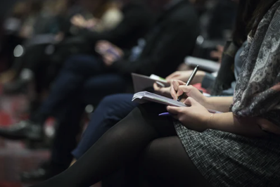 people writing in notebooks sittng at a conference.