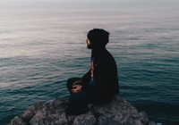 Man sitting on rick by water thinking.