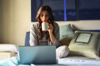 Woman in Grey Jacket Sits on Bed Uses Grey Laptop Free Stock Photo