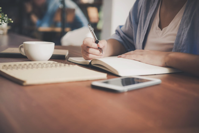 Woman Writing on a Notebook Beside Teacup and Tablet Computer Free Stock Photo